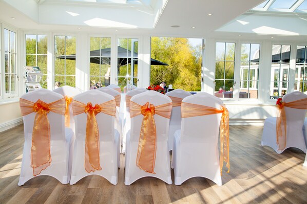 A spacious indoor venue with rows of white chairs adorned with orange sashes, large windows, and a wooden floor. - Rose and Crown Hotel (Salisbury)