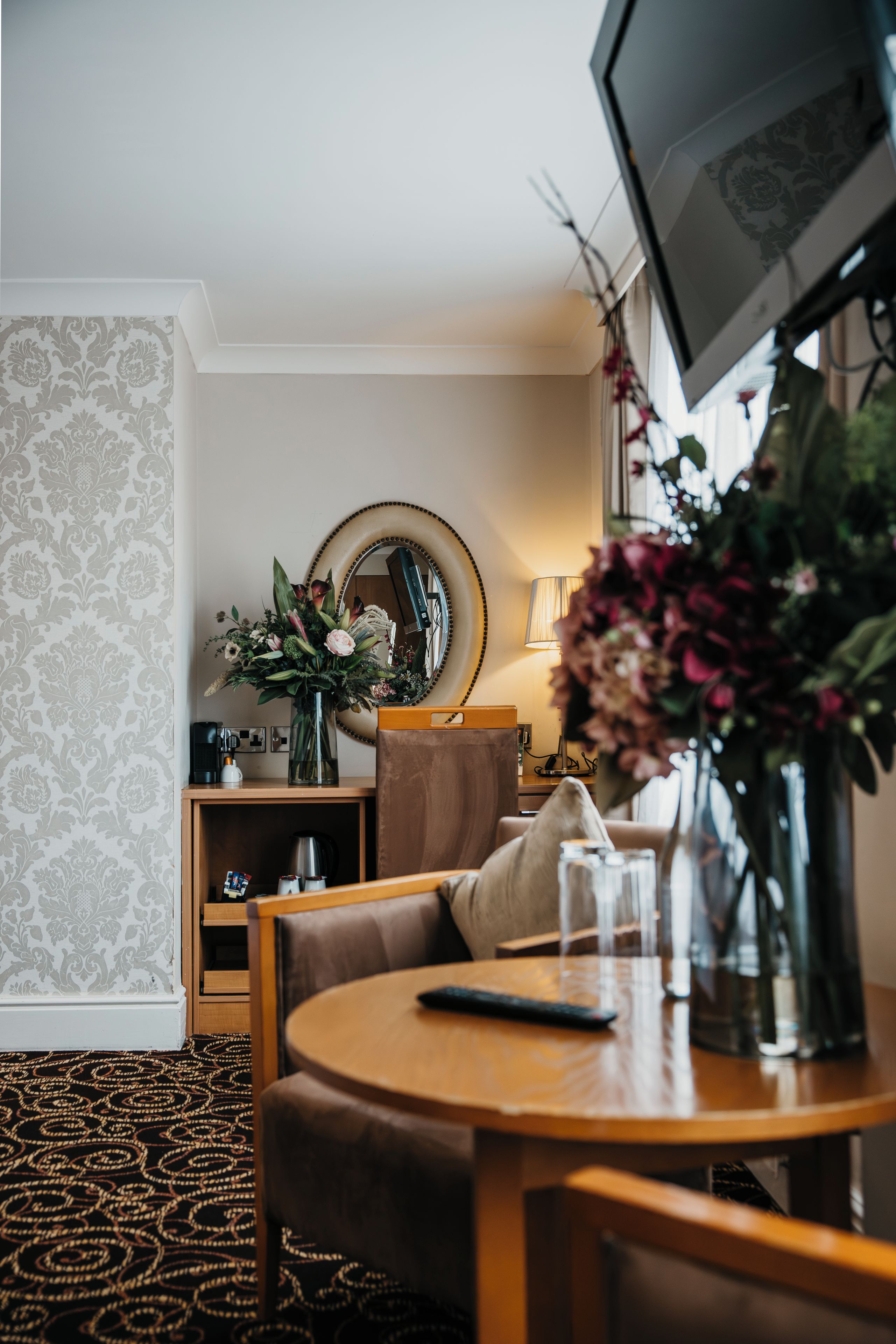 Habitación de hotel con una mesa de comedor, un sofá, un televisor y un espejo.