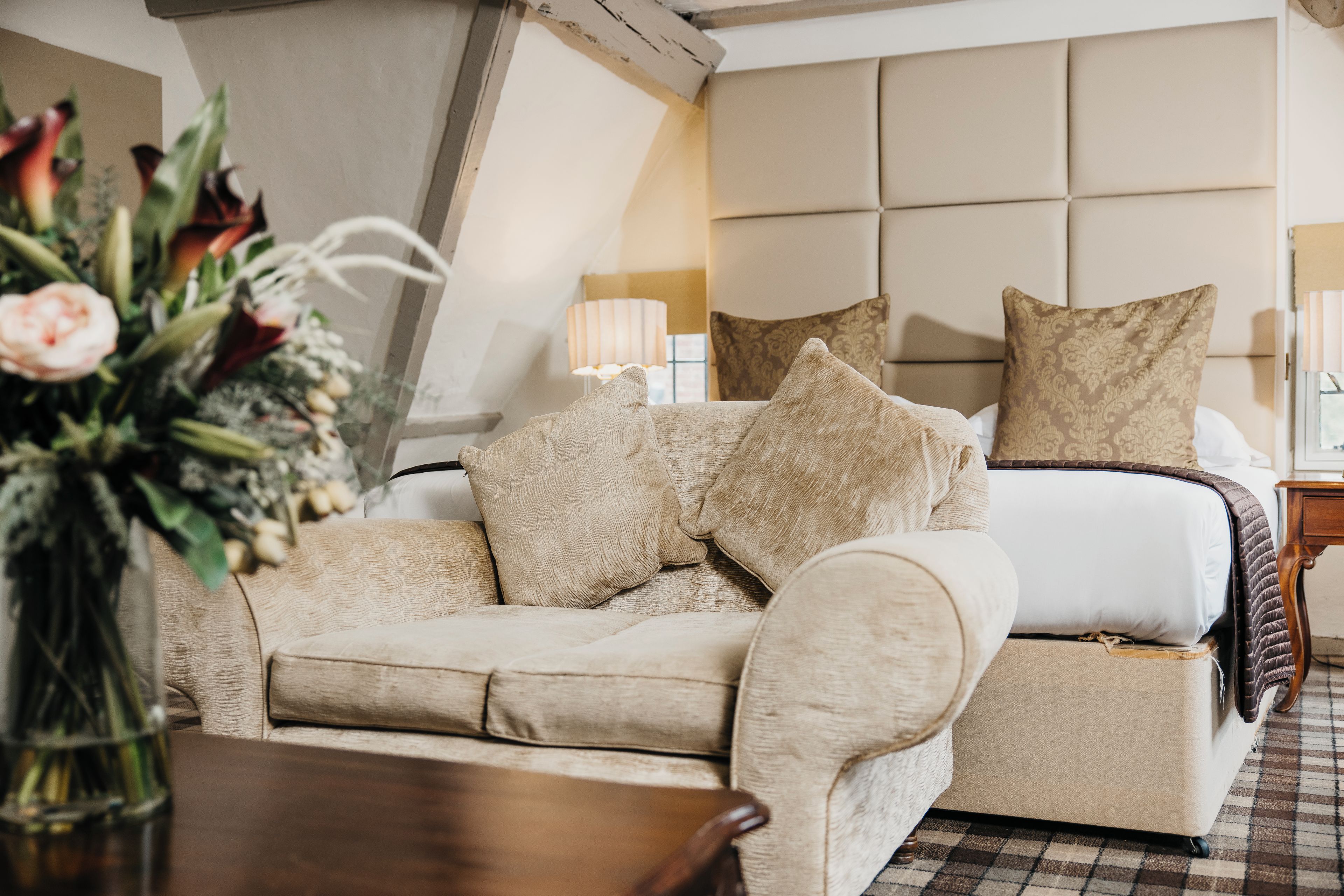 A hotel room with a bed, a sofa, a nightstand, and a lamp.
