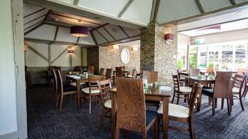 Un restaurante con mesas y sillas de madera, paredes de piedra y un gran reloj.