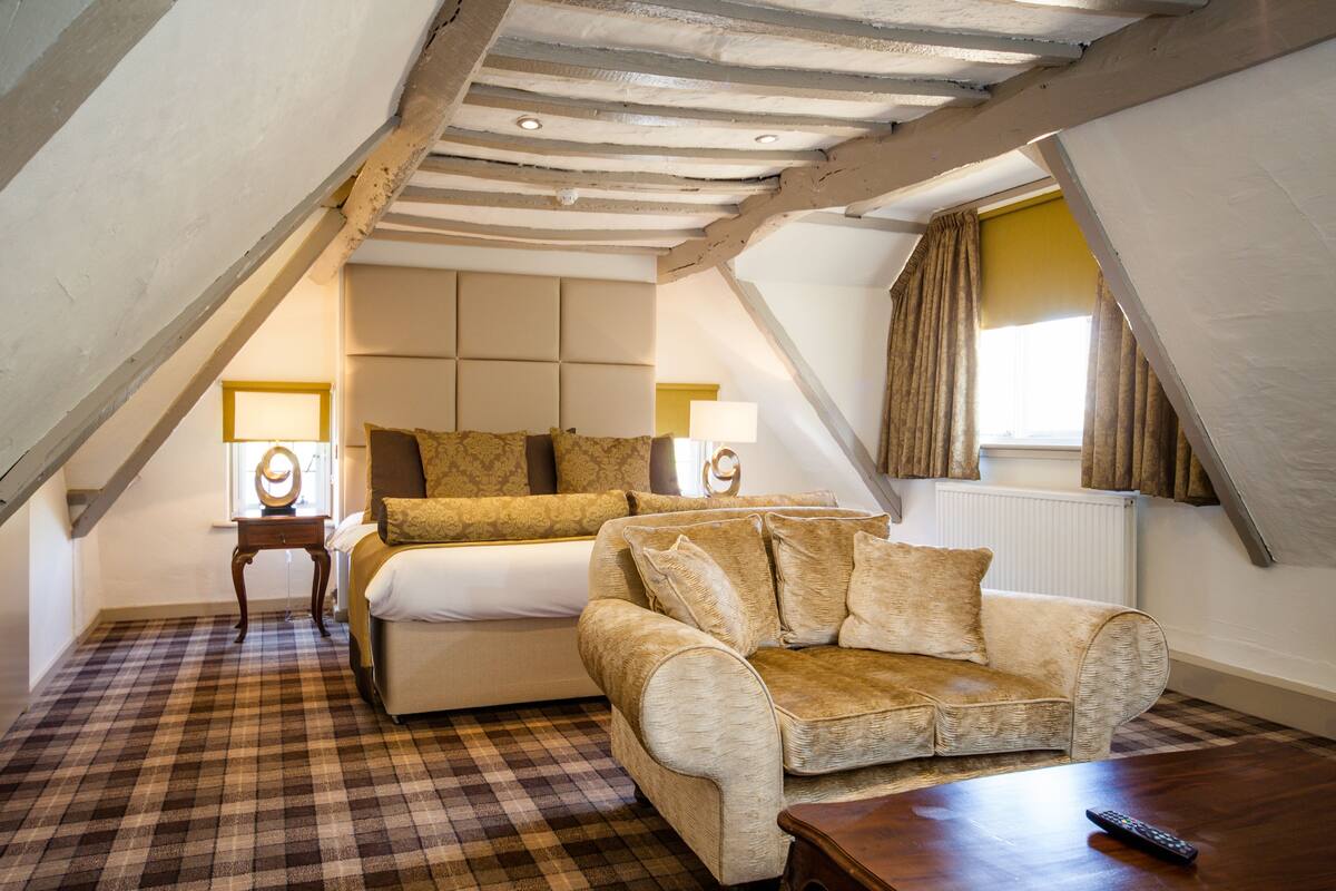 A cozy attic bedroom with a checkered floor, a bed, a sofa, and a wooden table.