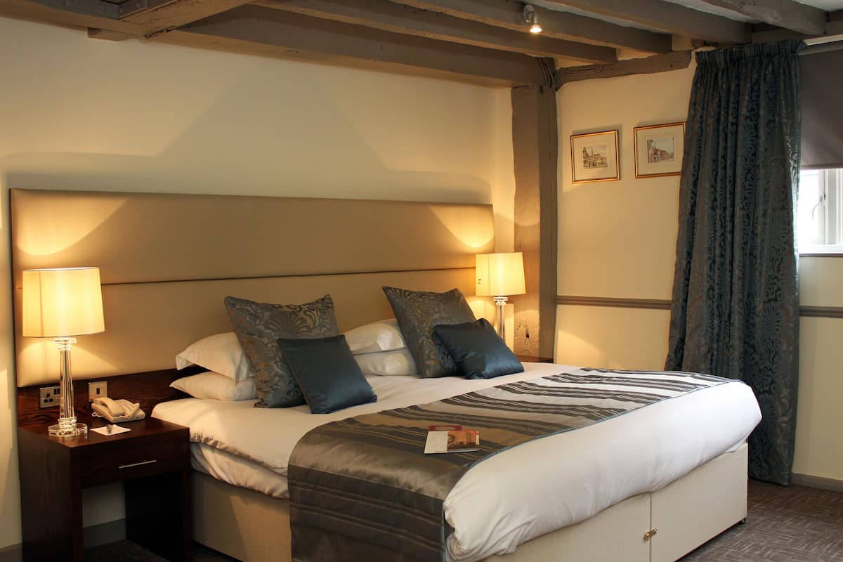A hotel room with a large bed, two bedside lamps, a nightstand, and a window with curtains.