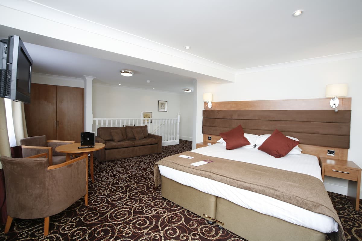 A hotel room with a bed, a sofa, a small table, and a TV.