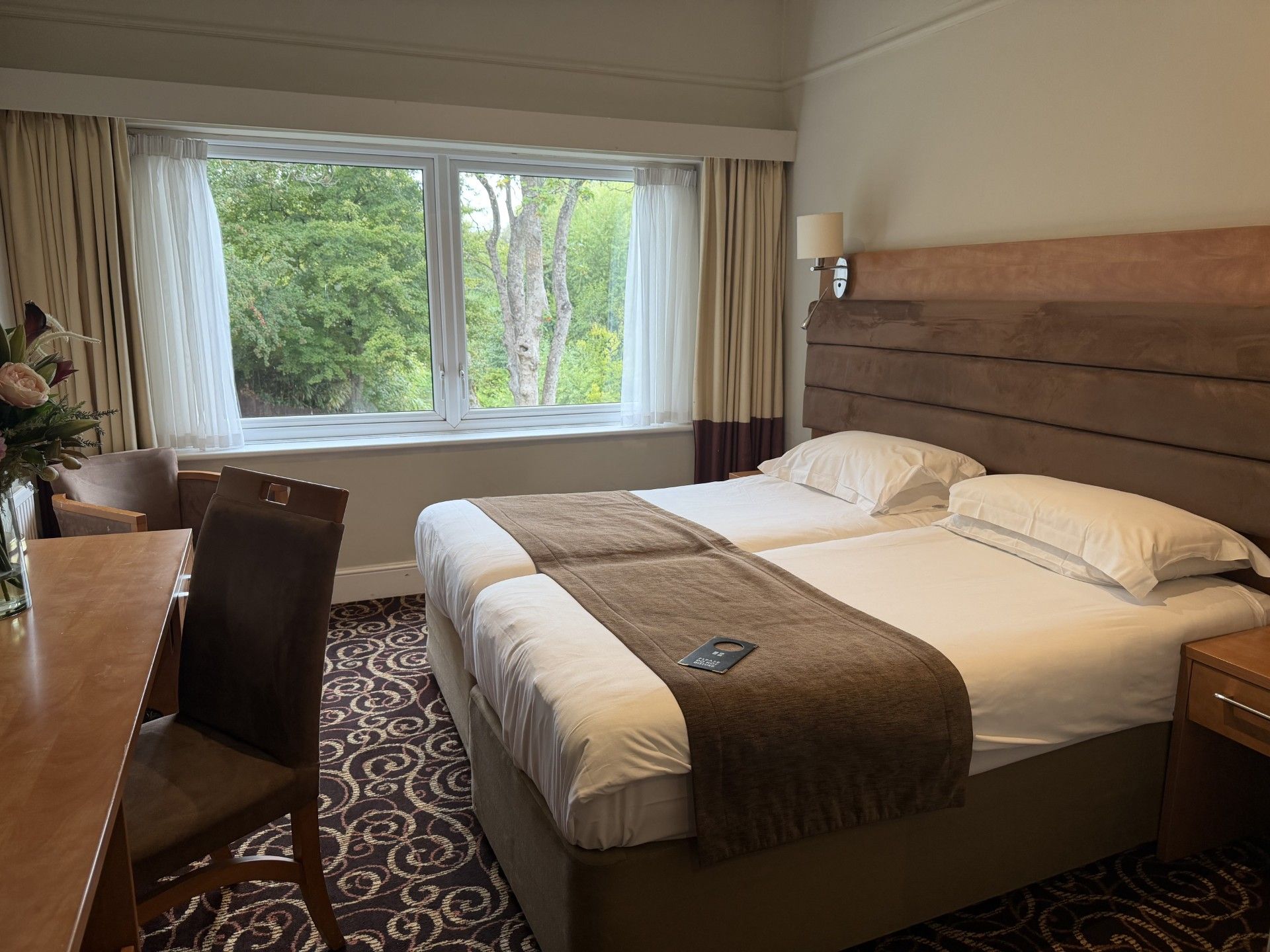 A hotel room with a bed, a desk, a chair, and a window with curtains.