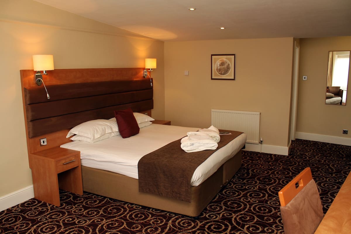 A hotel room with a large bed, two bedside tables, a headboard, a radiator, a carpeted floor, and a mirror on the wall.