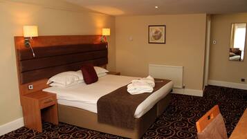 A hotel room with a large bed, two bedside tables, a headboard, a radiator, a carpeted floor, and a mirror on the wall.