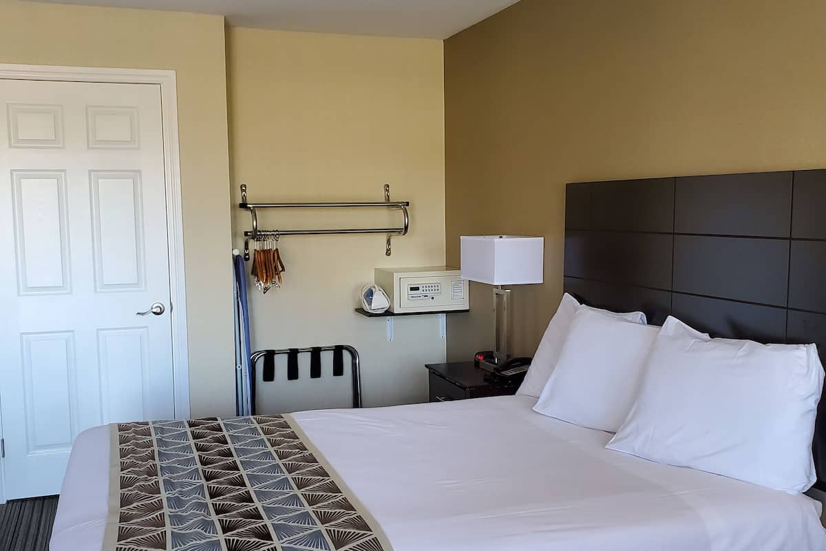Ein Hotelzimmer mit einem großen Bett, einem Nachttisch mit Lampe, einem Thermostat und einem an der Wand befestigten Handtuchhalter.