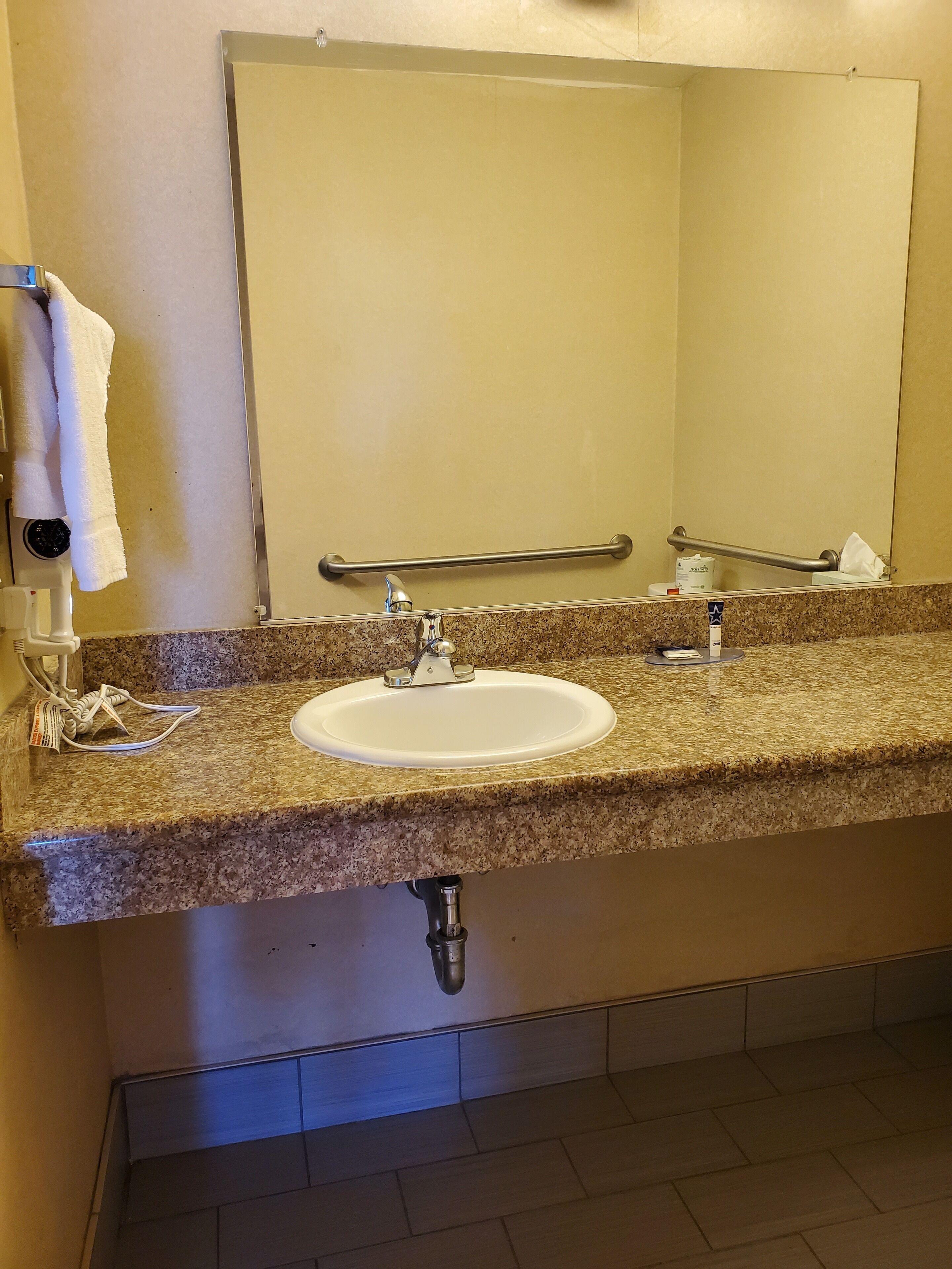 A bathroom with a granite countertop, a white sink, a mirror, a towel rack, and a hand dryer.