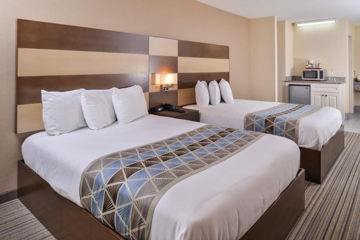Ein Hotelzimmer mit zwei Betten, einem Nachttisch, einer Lampe, einer Mikrowelle und einer kleinen Küchenzeile.