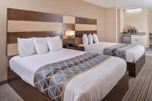 Une chambre d’hôtel avec deux lits, une table de chevet, une lampe, un four à micro-ondes et une petite kitchenette.