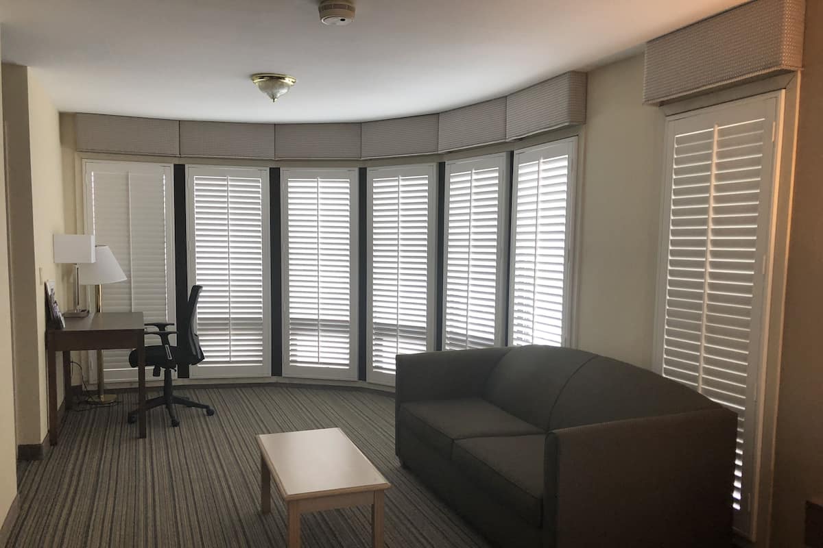 Ein Hotelzimmer mit großem Fenster, einer Couch, einem kleinen Tisch und einem Schreibtisch mit Lampe.