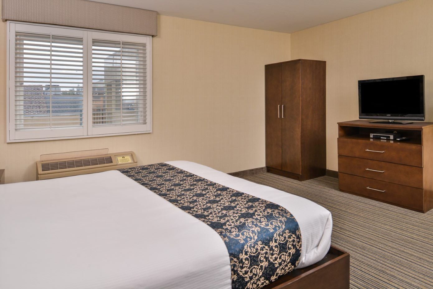 A hotel room with a bed, a wardrobe, a television, and a radiator.