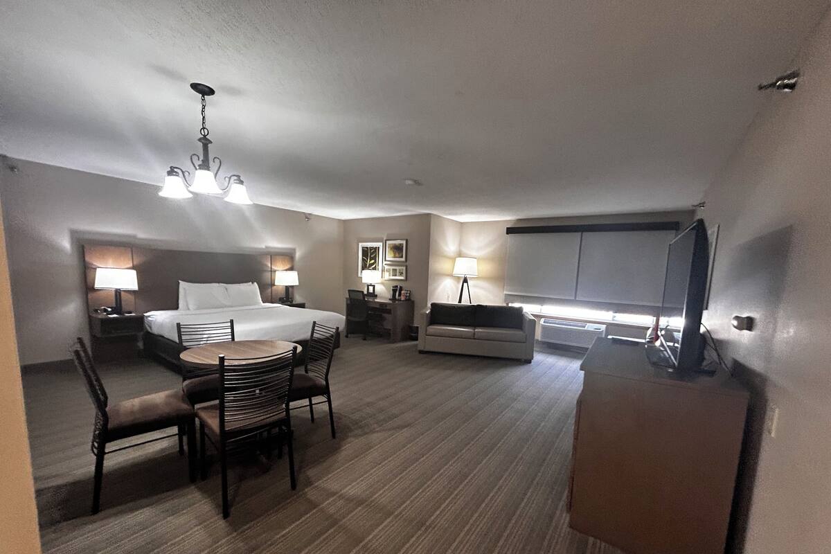A hotel room with a bed, desk, chair, dining table, and a television.