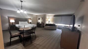 A hotel room with a bed, desk, chair, dining table, and a television.