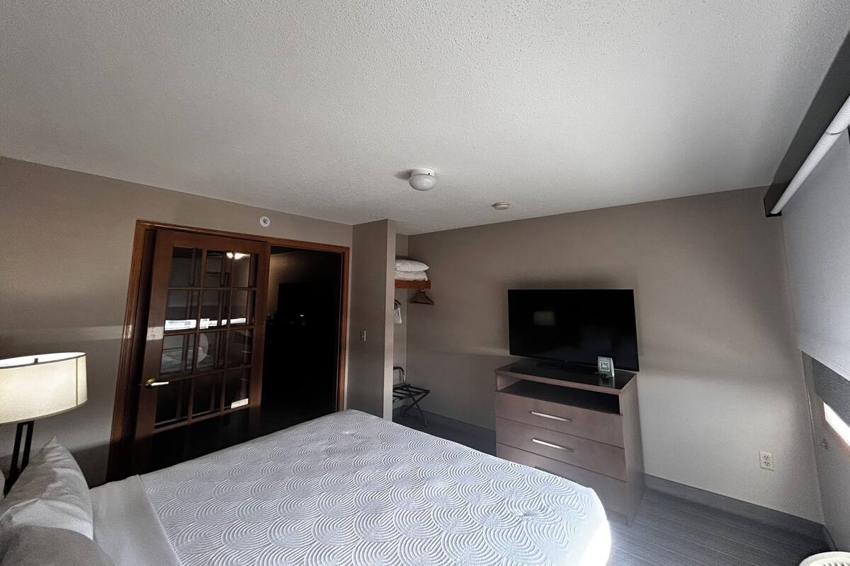A hotel room with a bed, a TV, a dresser, and a door leading to another room.