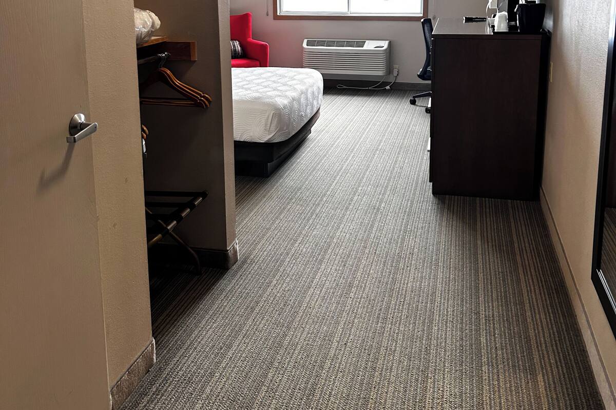 A hotel room with a bed, a desk, a chair, a wardrobe, and a window with a view of buildings.