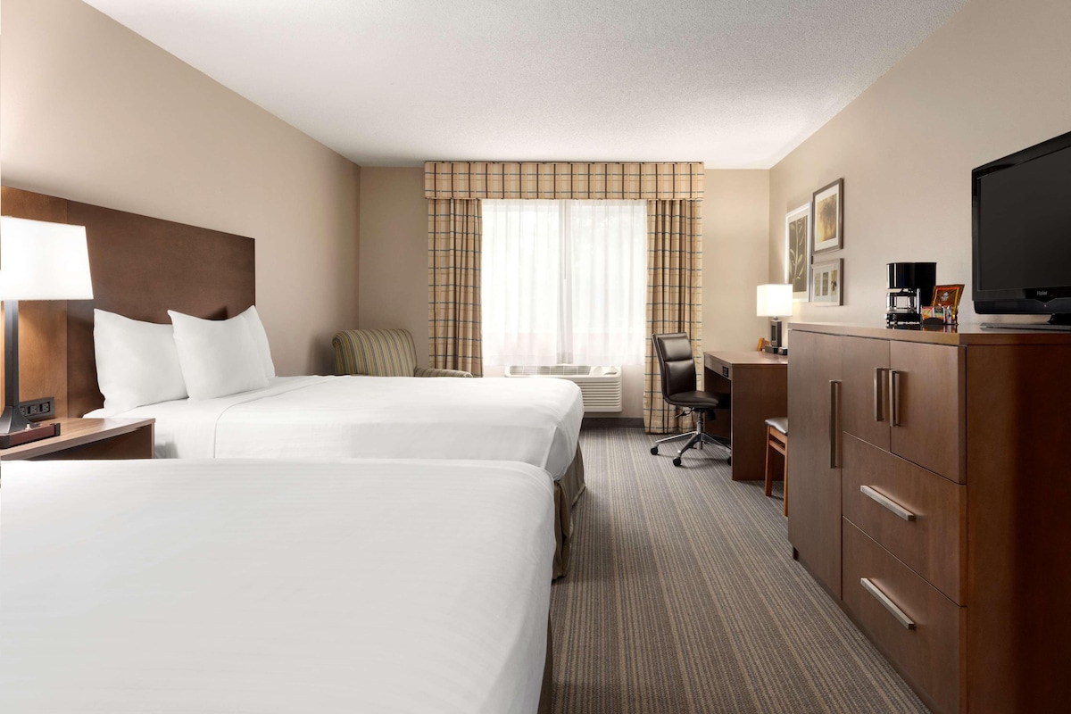 A hotel room with two beds, a desk, a chair, a television, and a wardrobe.