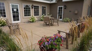 A covered patio area with a table and chairs, surrounded by potted plants and a flower bed. - Country Inn & Suites by Radisson, Baxter, MN (Brainerd)