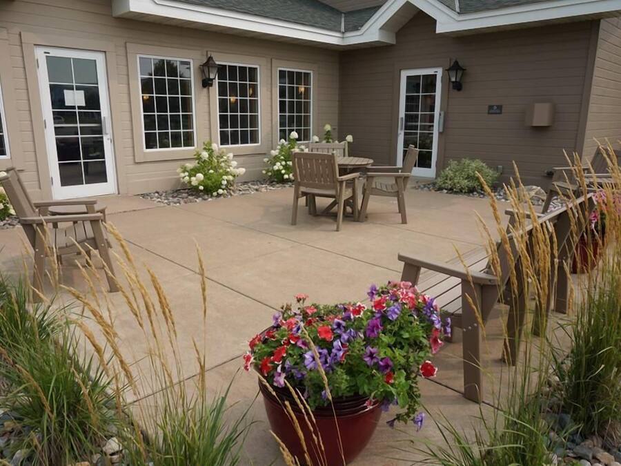 A covered patio area with a table and chairs, surrounded by potted plants and a flower bed.