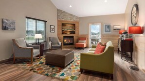 A spacious living room with a fireplace, comfortable seating, and a large window providing a view. - Country Inn & Suites by Radisson, Baxter, MN (Brainerd)