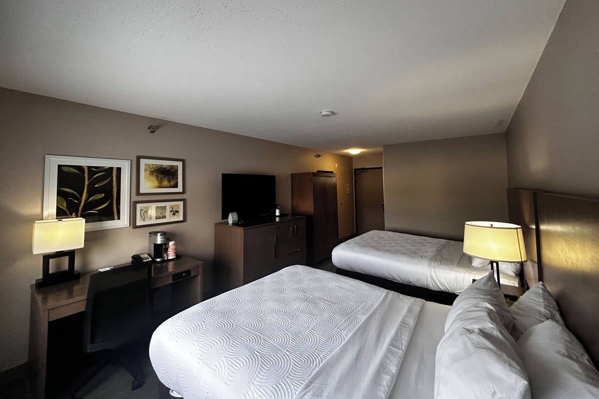 A hotel room with two beds, a desk with a lamp, a TV, and framed pictures on the wall.