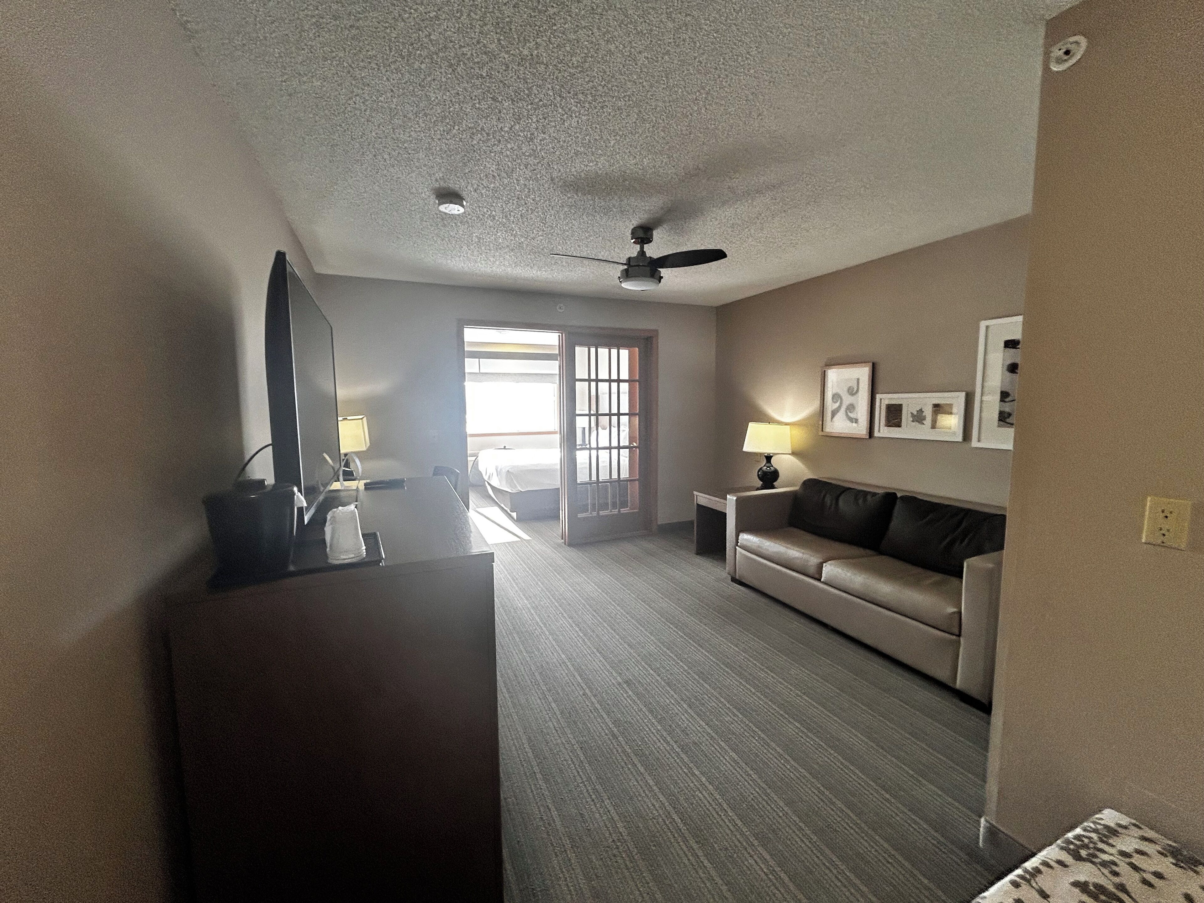 Une chambre d’hôtel équipée d’un bureau, d’un canapé, d’un ventilateur de plafond, d’un lit et d’une porte donnant sur un balcon.