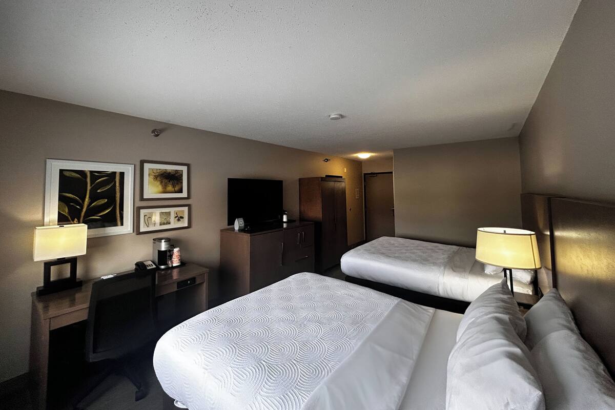 A hotel room with two beds, a desk with a lamp, a TV, and framed artwork on the wall.