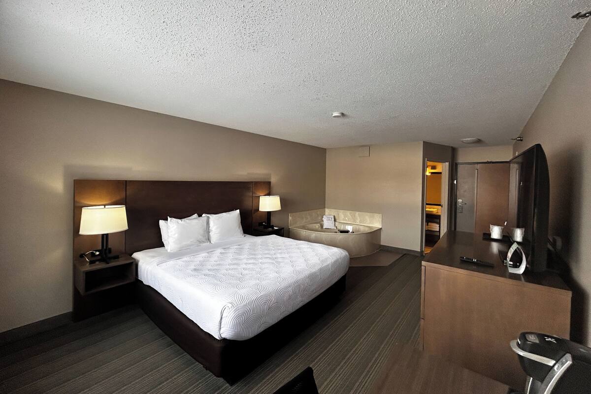 A hotel room with a large bed, two bedside lamps, a round mirror, a desk, and a walk-in closet.