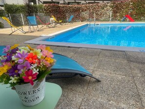 A swimming pool with lounge chairs and a flower arrangement on a table.