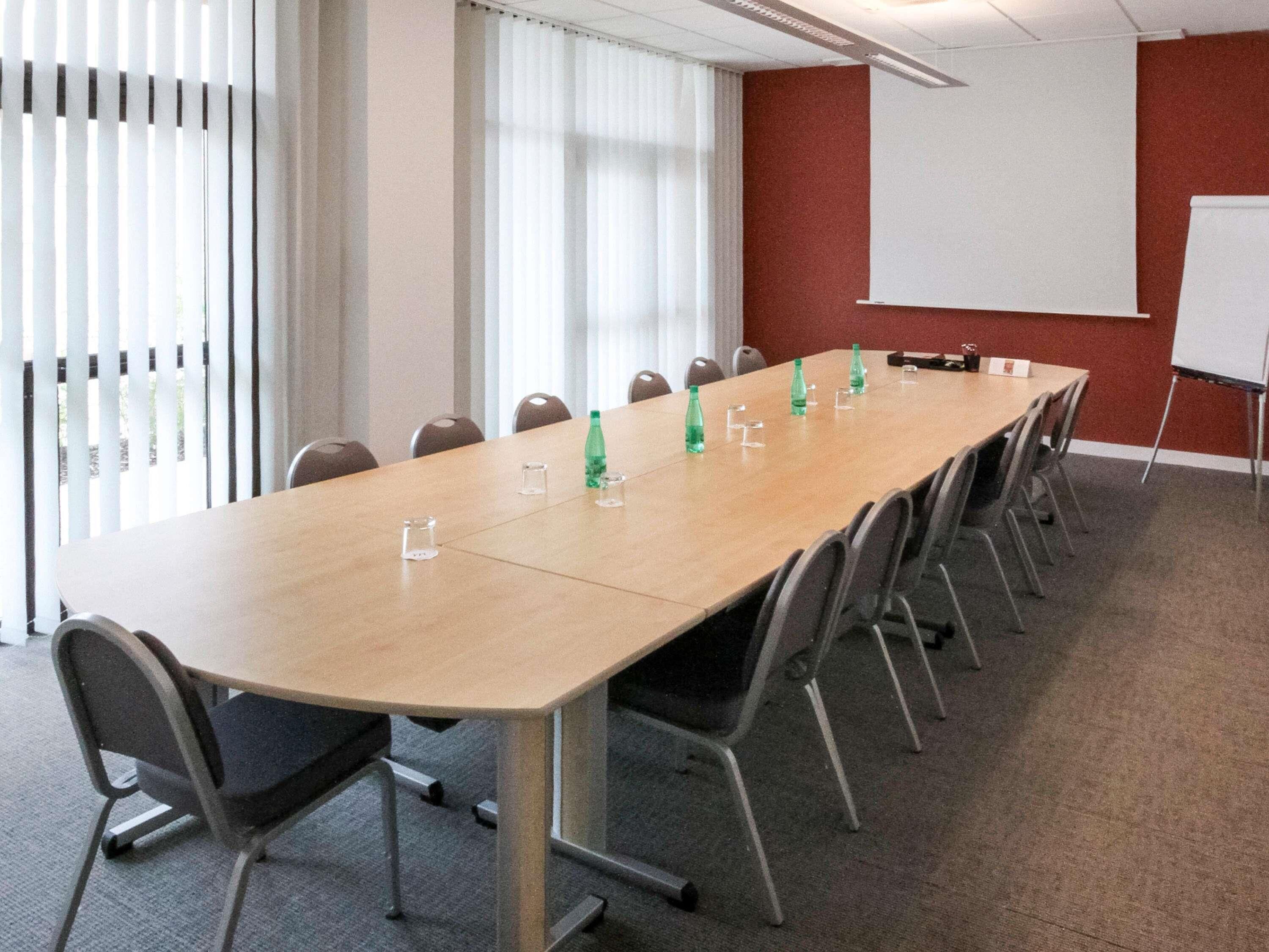 Un salón de conferencias con una larga mesa, sillas, una pizarra y una pantalla de proyector.