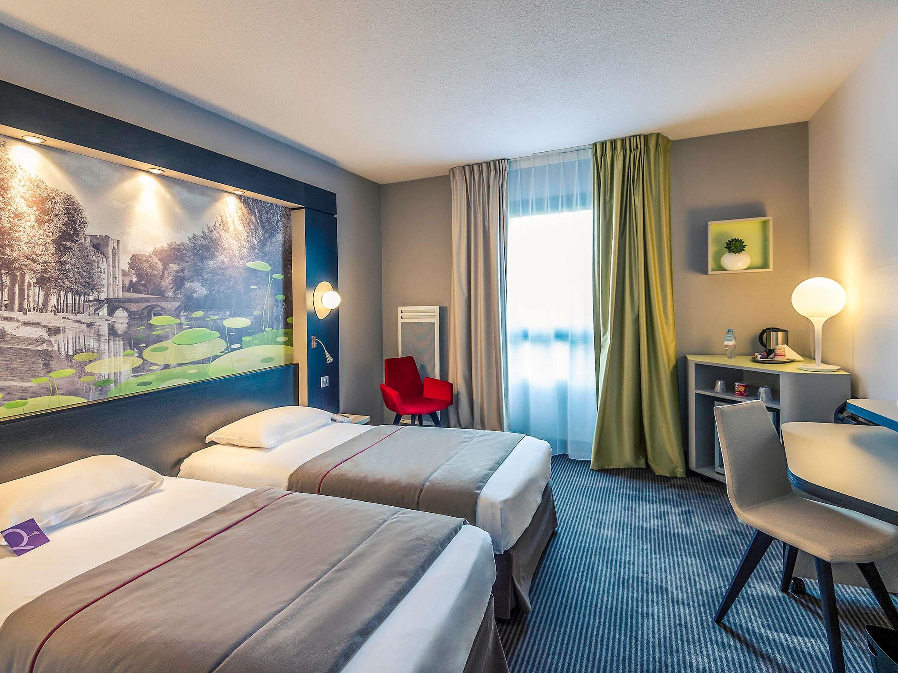 A hotel room with two beds, a desk, a chair, a lamp, and a painting on the wall.