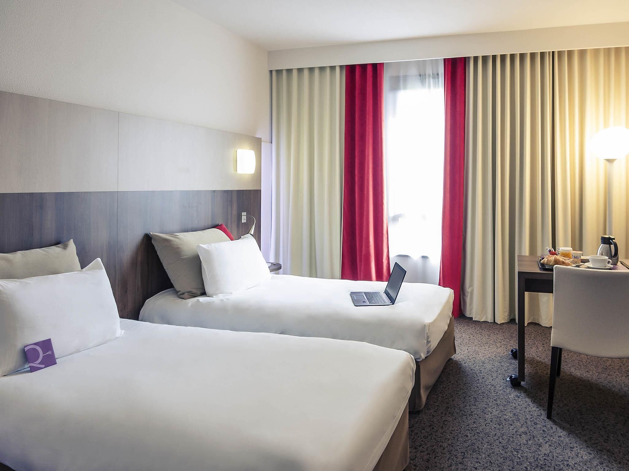 A hotel room with two beds, a desk with a laptop, a coffee maker, and a chair.
