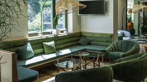 Un área de estar moderna con un sofá verde, sillones y mesas de vidrio.