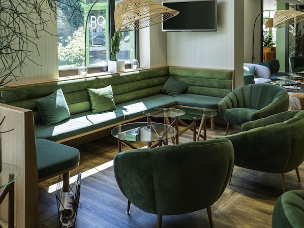 A modern lounge area with a green sofa, armchairs, and glass tables.