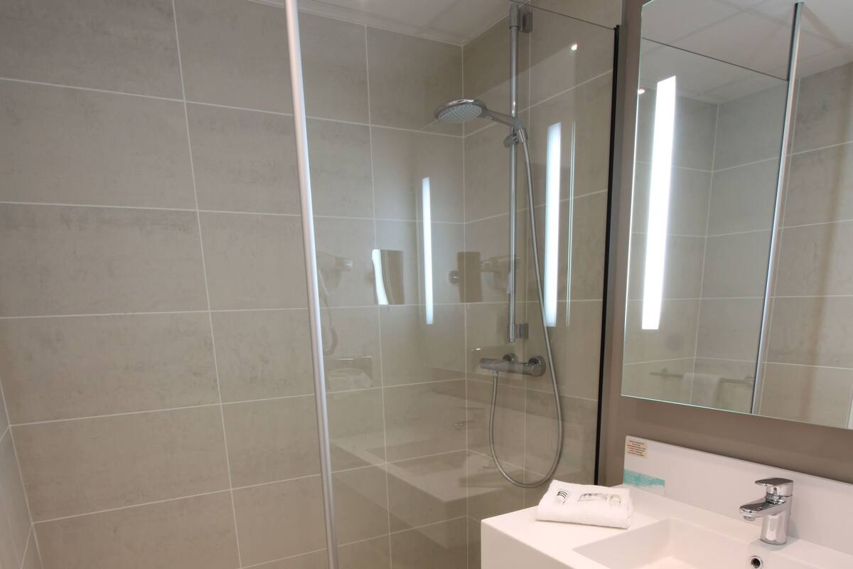 A modern bathroom with a glass-enclosed shower, a white sink, and a large mirror.