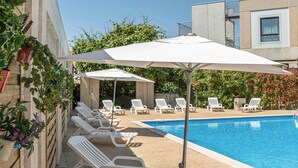Zona de piscina con sillas de descanso y sombrillas.