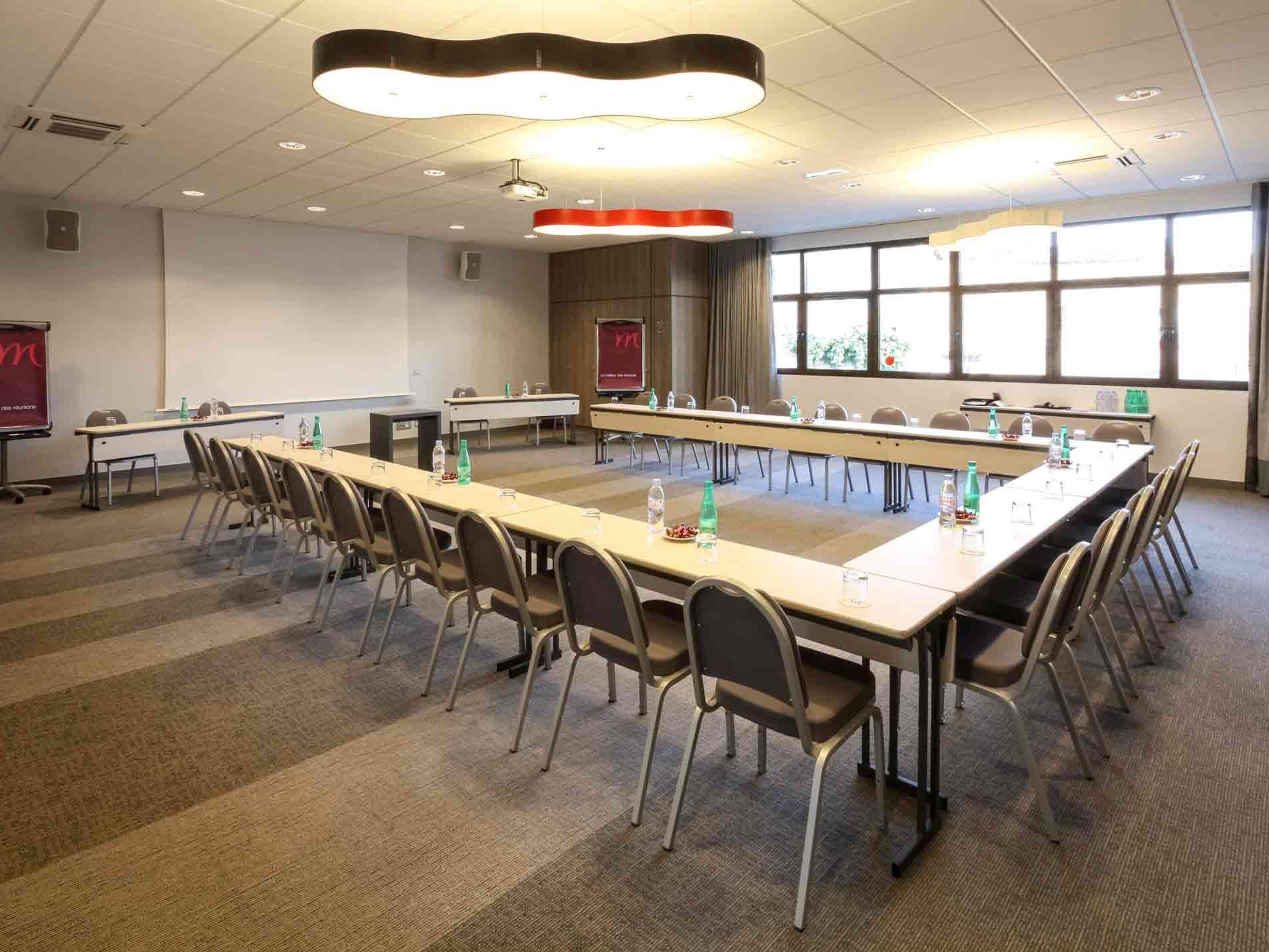A conference room with a long table, chairs, a projector screen, and large windows.
