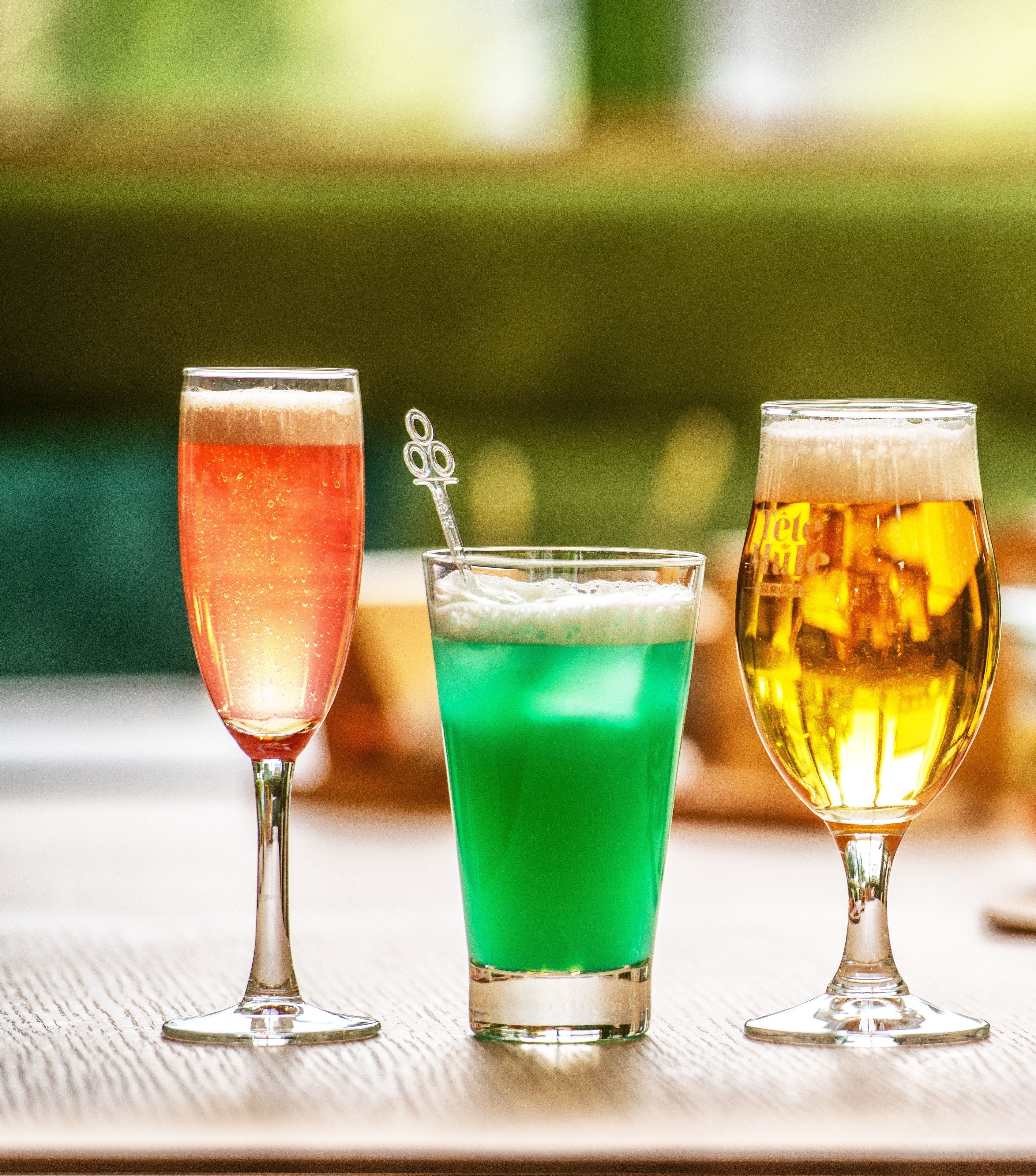 Three glasses of different colored beverages on a wooden table.