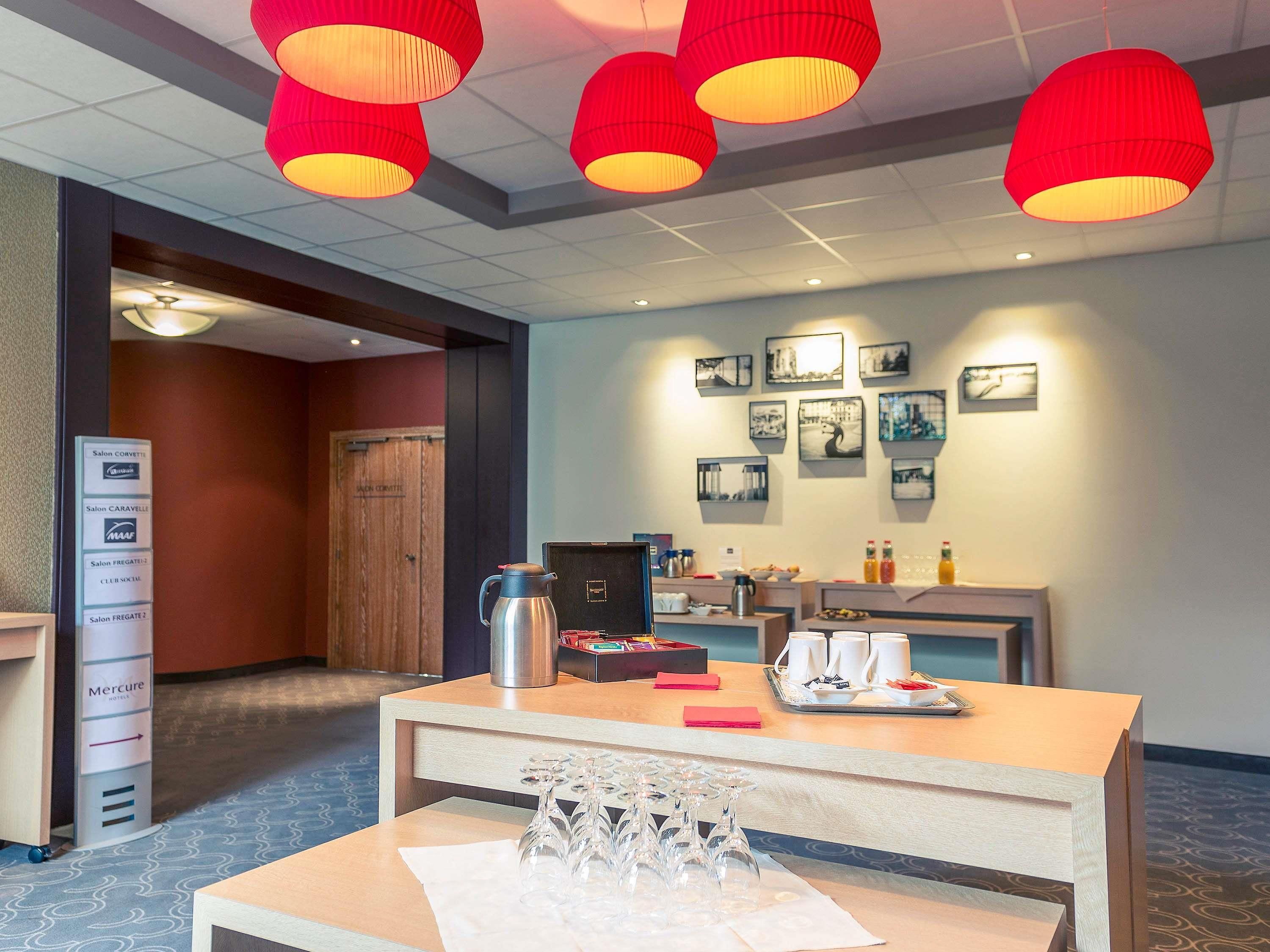 Un espace d’accueil d’hôtel comprenant un comptoir de réception, un coin café et un mur orné de tableaux.