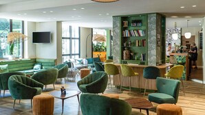 Un área de estar moderna con sillones tapizados en verde, una mesa de centro de madera y una estantería verde con libros y objetos decorativos.