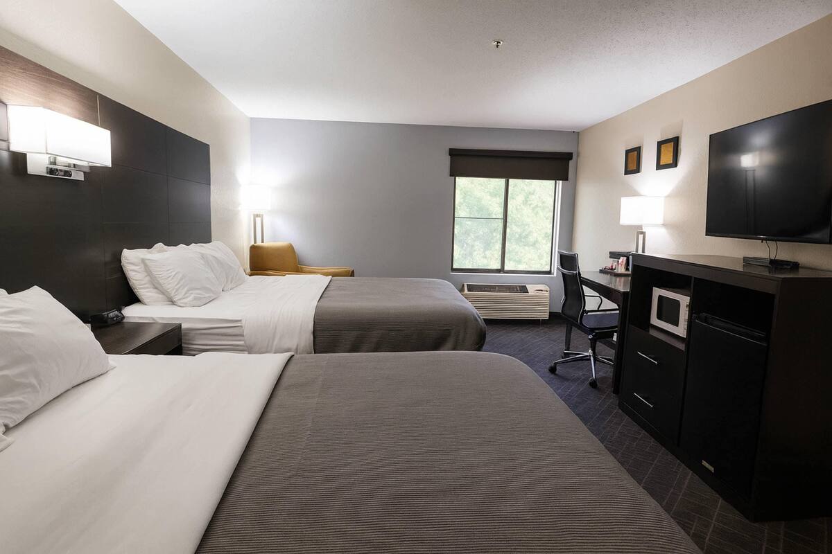 Quarto de hotel com duas camas, uma escrivaninha, televisão e janela.