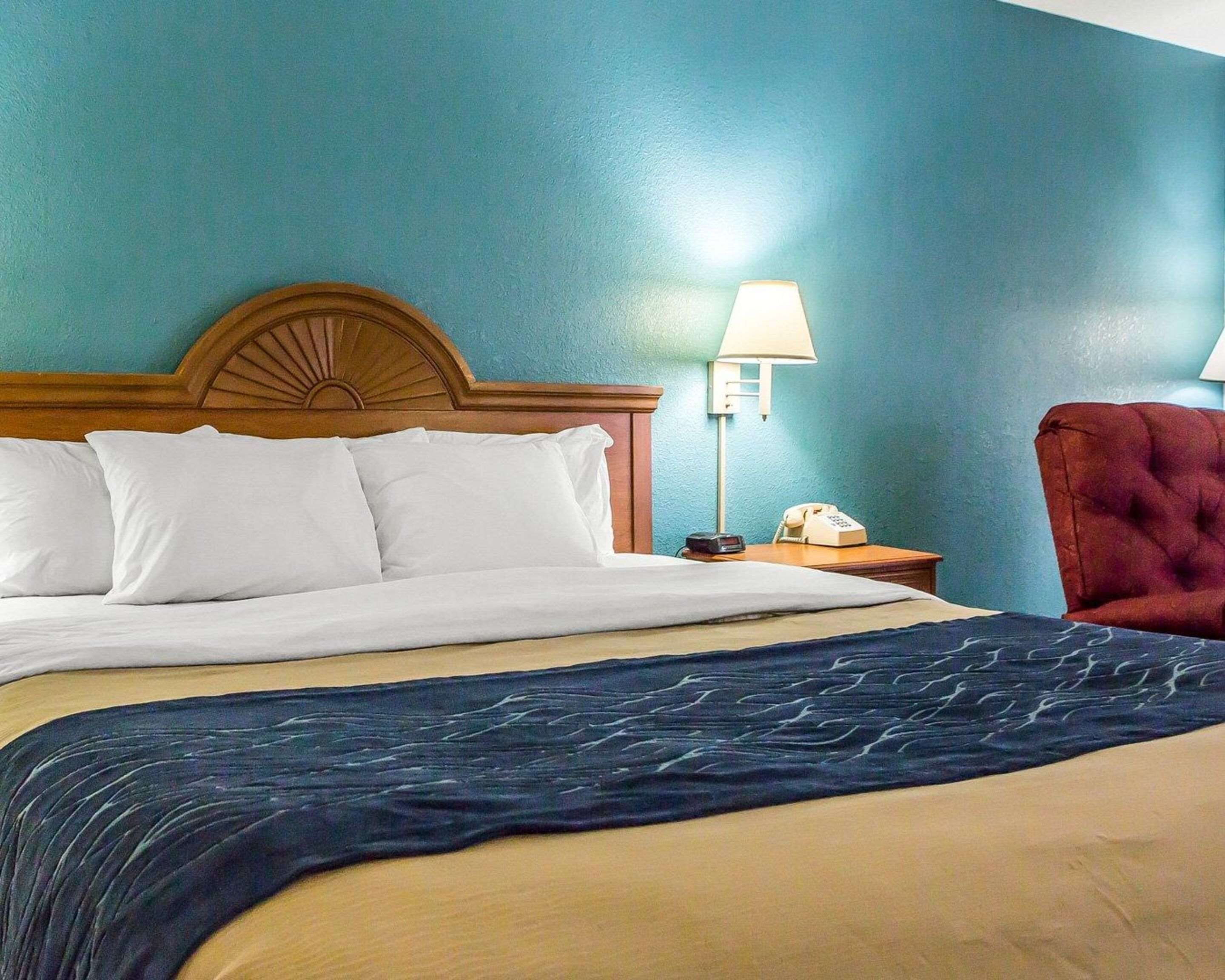 Habitación de hotel con una cama, una mesita de noche con lámpara, un teléfono y una silla roja.