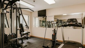Un gimnasio con equipo de ejercicio diverso, una cinta de correr y un televisor montado en la pared.