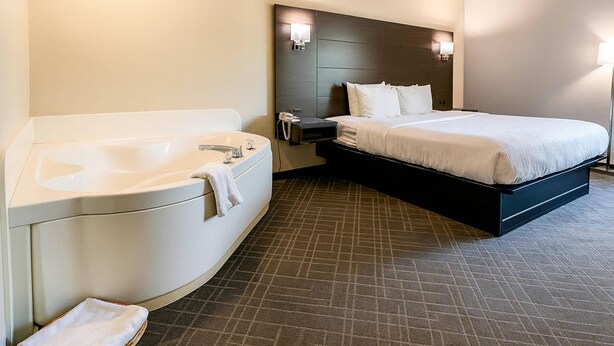 Una habitación de hotel con una bañera grande, una cama con sábanas blancas y un cabecero oscuro.