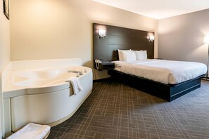 Quarto de hotel com uma banheira grande, cama com roupa de cama branca e cabeceira escura.