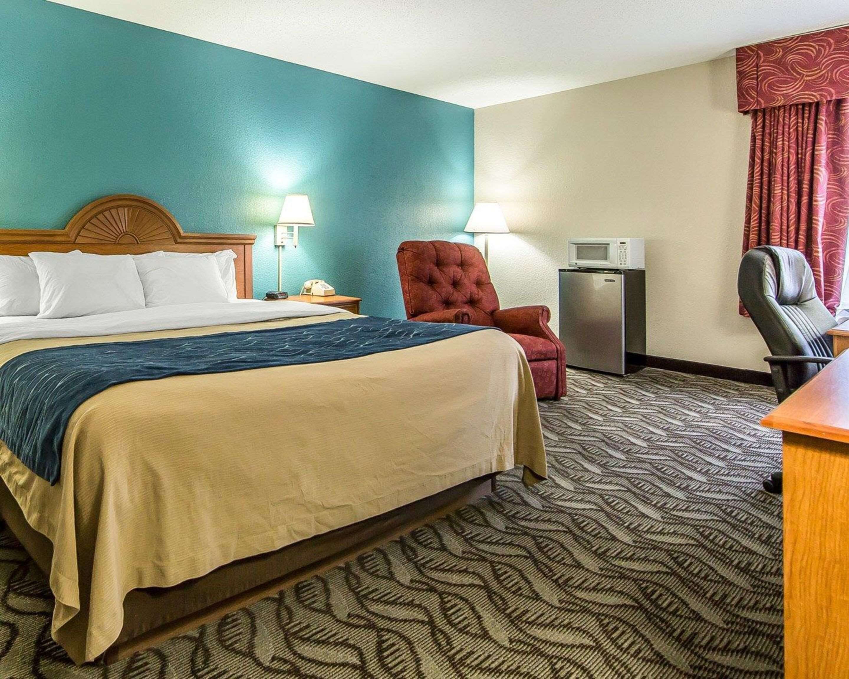 Habitación de hotel con cama, escritorio, silla, lámpara y microondas.