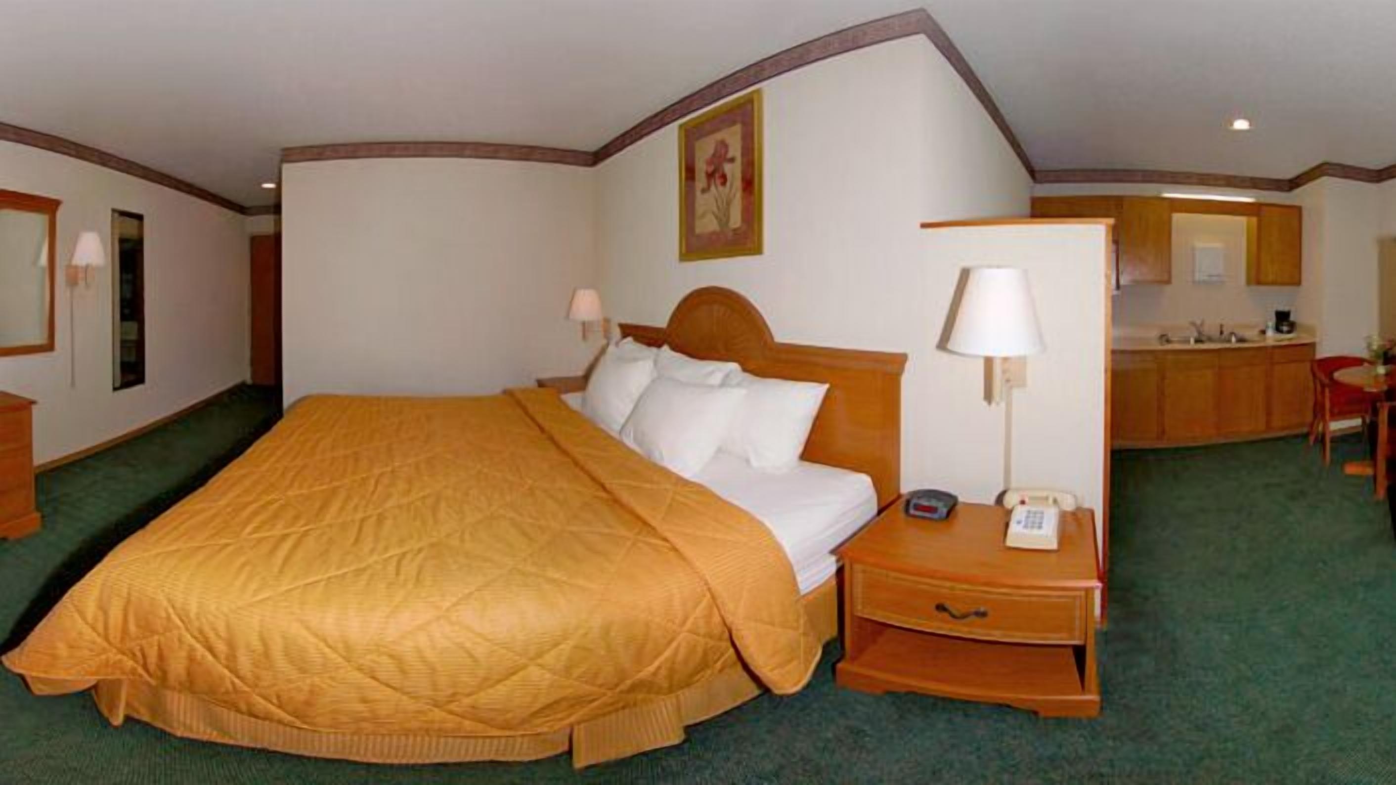 A hotel room with a large bed, a bedside table with a lamp, a phone, and a small desk with a chair.