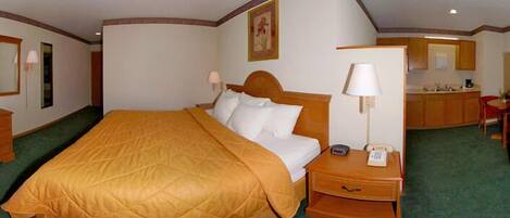A hotel room with a large bed, a bedside table with a lamp, a phone, and a small desk with a chair.