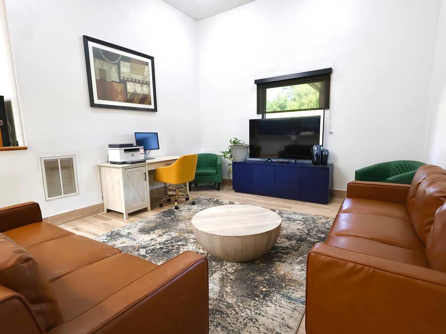 A modern living room with a brown leather sofa, a round coffee table, a yellow chair, a blue entertainment unit, and a framed artwork on the wall.