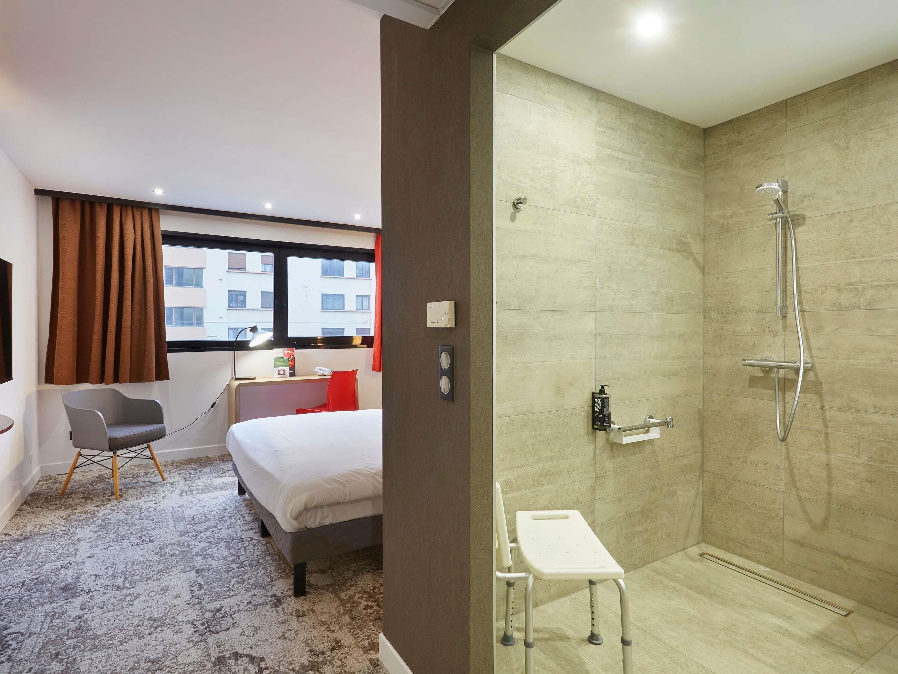 Habitación de hotel con cama, escritorio, silla, una mesita pequeña y zona de ducha.